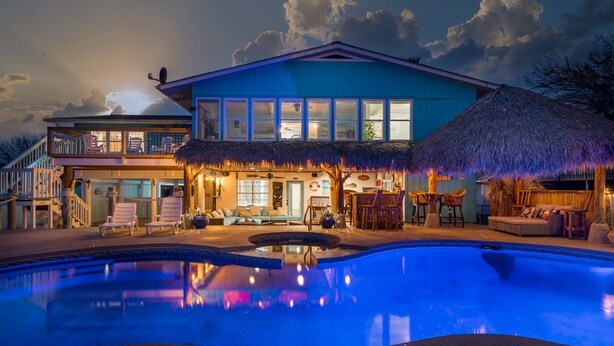 A large house with a swimming pool, a covered outdoor area with seating, and a thatched-roof structure. - Texas Tiki by Miss Kitty’s (Rockport)