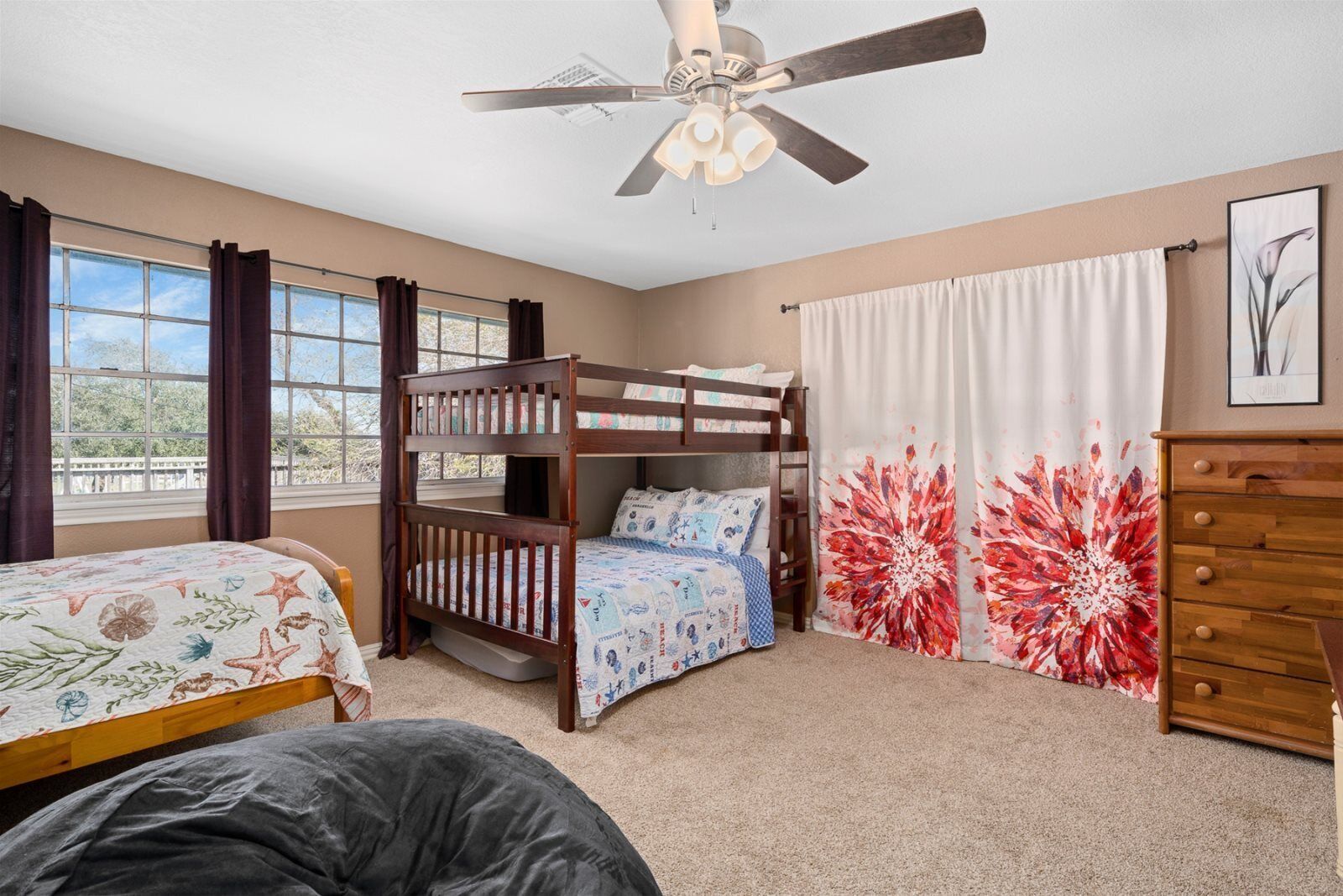 Une chambre avec un lit superposé, un ventilateur de plafond, une commode et une fenêtre avec des rideaux.