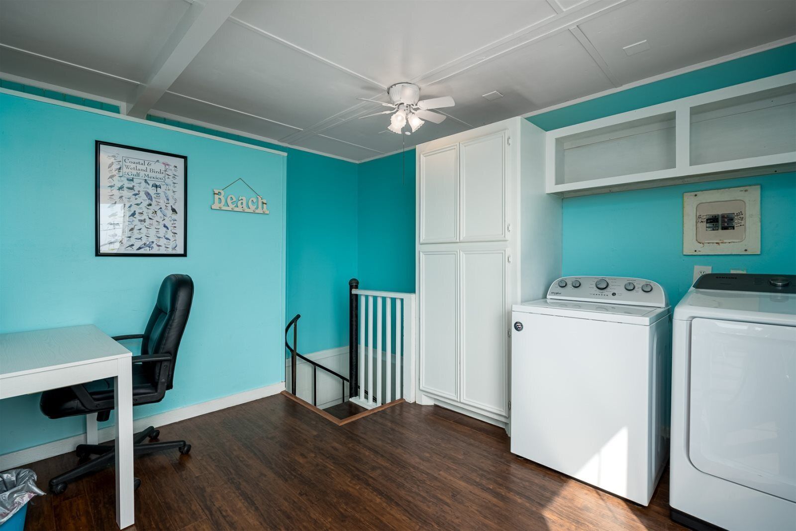 A laundry room with a washing machine and dryer, a chair, a small table, and a ceiling fan.
