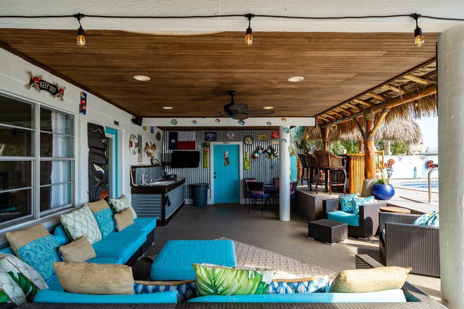 A covered outdoor seating area with a kitchen, a blue door, and tiki decorations.