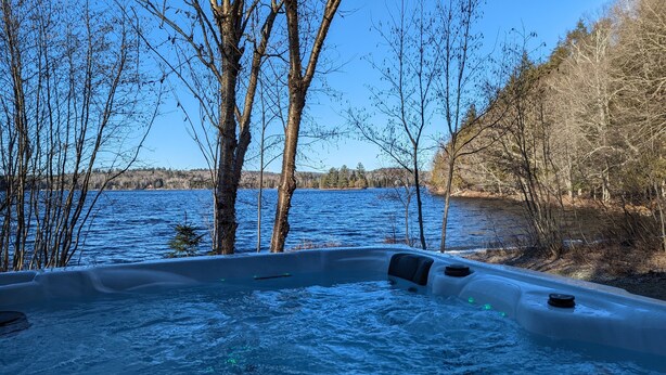 A hot tub surrounded by trees and a body of water. - The Starry beach, lake front cottage (Amherst)