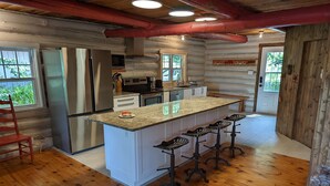 A log cabin kitchen with a central island, bar stools, a refrigerator, and a microwave. - The Starry beach, lake front cottage (Amherst)
