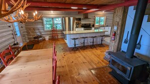 A log cabin interior with a wooden dining area, kitchen, and a wood-burning stove. - The Starry beach, lake front cottage (Amherst)