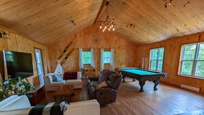 A cozy wooden cabin interior with a pool table, sofas, and a television. - The Starry beach, lake front cottage (Amherst)
