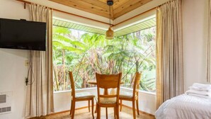 A room with a bed, a television, a dining table with chairs, and a large window with curtains. - Relaxing 2-bedroom Lodge in Volcano with Hot Tub (Mountain View)
