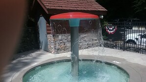 Una fuente de agua con un muro de piedra y un techo rojo al fondo.