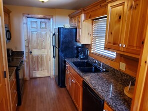 A kitchen with wooden cabinets, a black refrigerator, a sink, and a coffee maker.