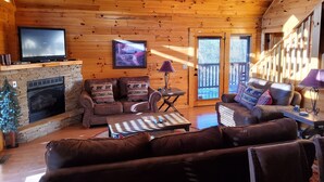 Un acogedor interior de cabaña con chimenea, sofás de cuero, un televisor y techo de madera.