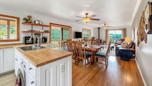 A spacious kitchen with wooden countertops, a dining area with wooden chairs, and a living room with a sofa and a TV.