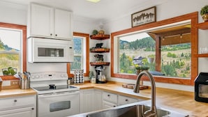 A modern kitchen with white cabinets, a stainless steel sink, and a large window offering a view of a mountainous landscape.