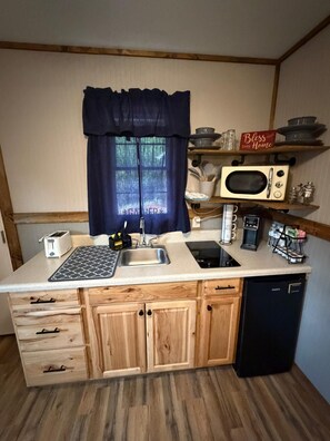 A compact kitchen with a sink, stove, microwave, and wooden cabinets.