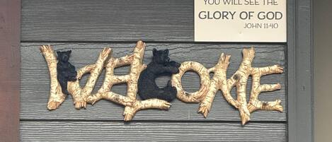 Een houten deur met een bord waarop staat 'IF YOU BELIEVE, YOU WILL SEE THE GLORY OF GOD' en een decoratief 'WELCOME'-bord.