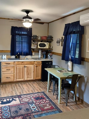 A compact kitchen with wooden cabinets, a microwave, a coffee maker, and a dining area with a table and chairs.