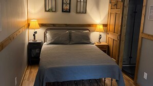 Un dormitorio con una cama, dos lámparas de noche, un ventilador de techo, una puerta de madera y una alfombra estampada.