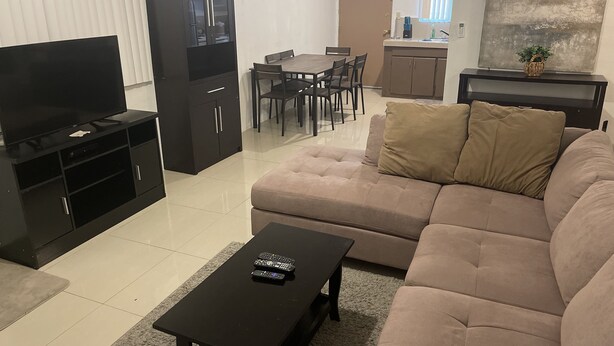 Un salon comprenant un canapé, un téléviseur, un meuble, une table à manger et des chaises.