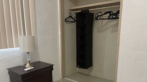Une pièce avec une commode en bois foncé, une lampe blanche, un organiseur suspendu noir et un placard équipé d’un autre organiseur suspendu noir.