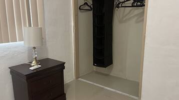 A room with a dark wooden dresser, a white lamp, a black hanging organizer, and a closet with a black hanging organizer.