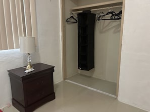A room with a dark wooden dresser, a white lamp, a black hanging organizer, and a closet with a black hanging organizer.
