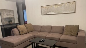 Un salon avec un canapé d’angle marron, une petite table basse noire et un tapis à longues mèches.