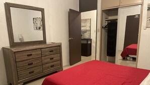 Une chambre à coucher avec une commode en bois, une couvre-lit rouge, un miroir et une armoire avec une couvre-lit rouge.