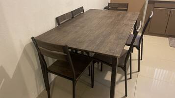 Una mesa rectangular para comedor con cuatro sillas, una zona de cocina con armarios y un piso con baldosas.