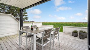 A wooden deck with a table and chairs, overlooking a grassy field. - Beautiful home in Gedser with kitchen (Gedser)