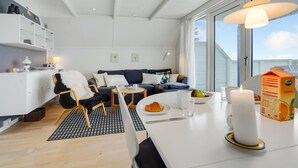 A modern, well-lit living room with a sofa, chairs, a dining table, and a large window offering a view. - Beautiful home in Gedser with kitchen (Gedser)