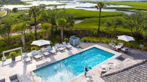 A rooftop pool with lounge chairs and umbrellas, surrounded by lush greenery and a view of a water body.