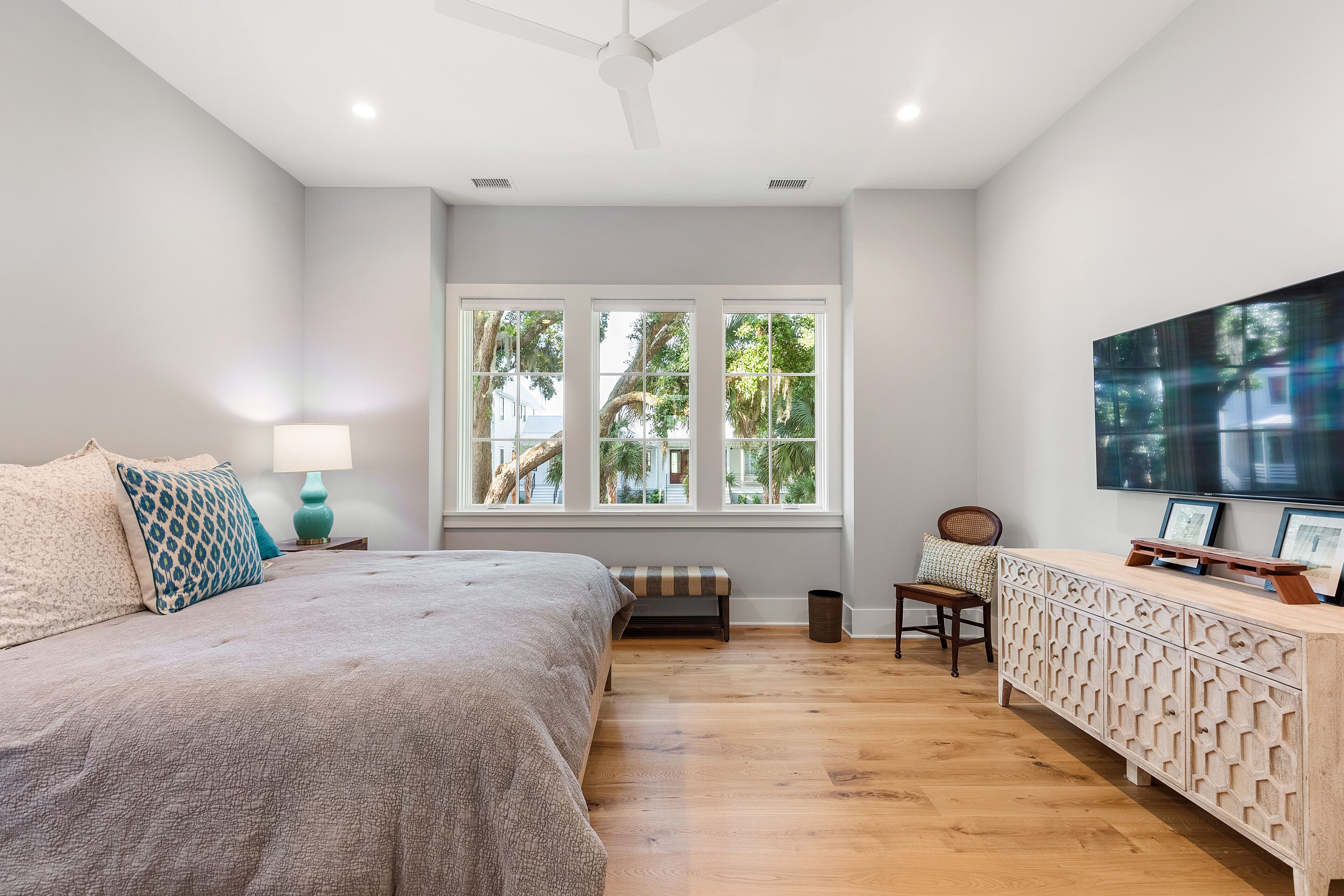 A bedroom with a bed, a nightstand, a lamp, a bench, a TV, and a cabinet.