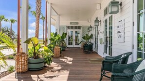 A covered porch with wooden flooring, potted plants, wicker chairs, and a sign reading "Welcome".