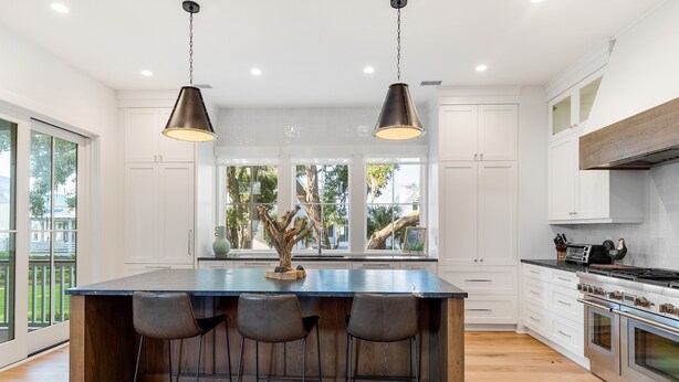 A modern kitchen with a large island, bar stools, pendant lighting, and a view of the outdoors.