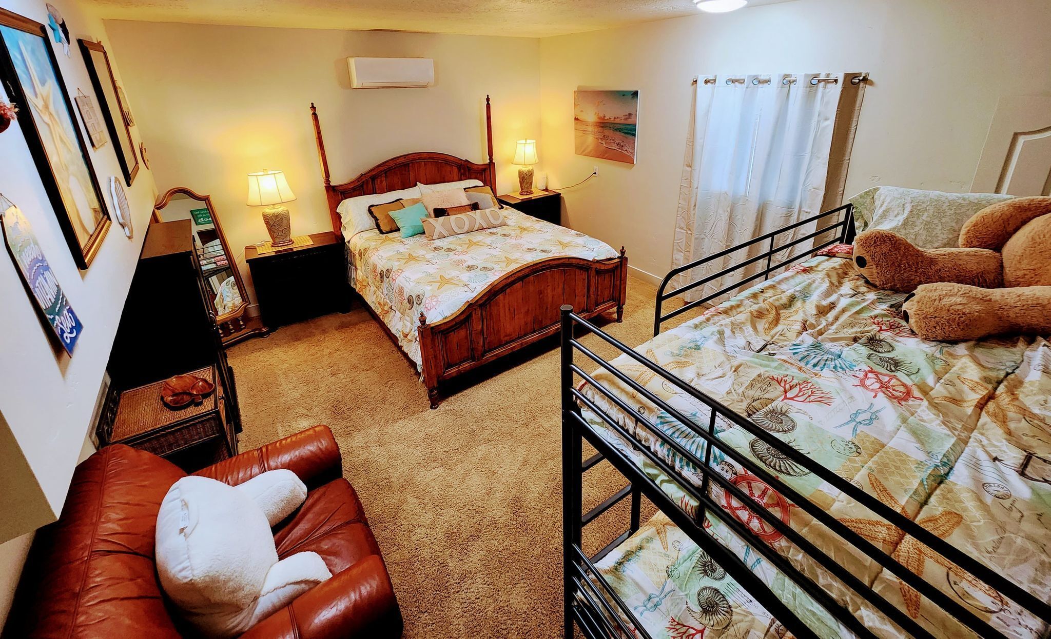 Une chambre confortable avec un lit en bois, un plus petit lit recouvert d’une courtepointe à motifs, un fauteuil en cuir rouge et un lit superposé avec une courtepointe sur le thème de la marine.