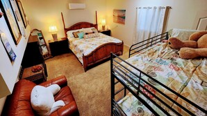 Ein gemütliches Schlafzimmer mit einem hölzernen Bett, einem weiteren Bett mit einem gemusterten Überwurf, einem roten Ledersessel und einem Etagenbett mit maritimer Bettwäsche.