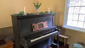 A grand piano in a room with a window, a small stool, and a wooden bench.