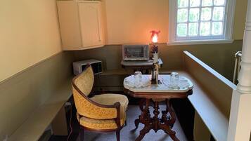 A corner room with a vintage chair, a table with candles, a microwave, and a window with a view.