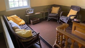 A cozy room with wicker furniture, a bench, and a window with a view of greenery.