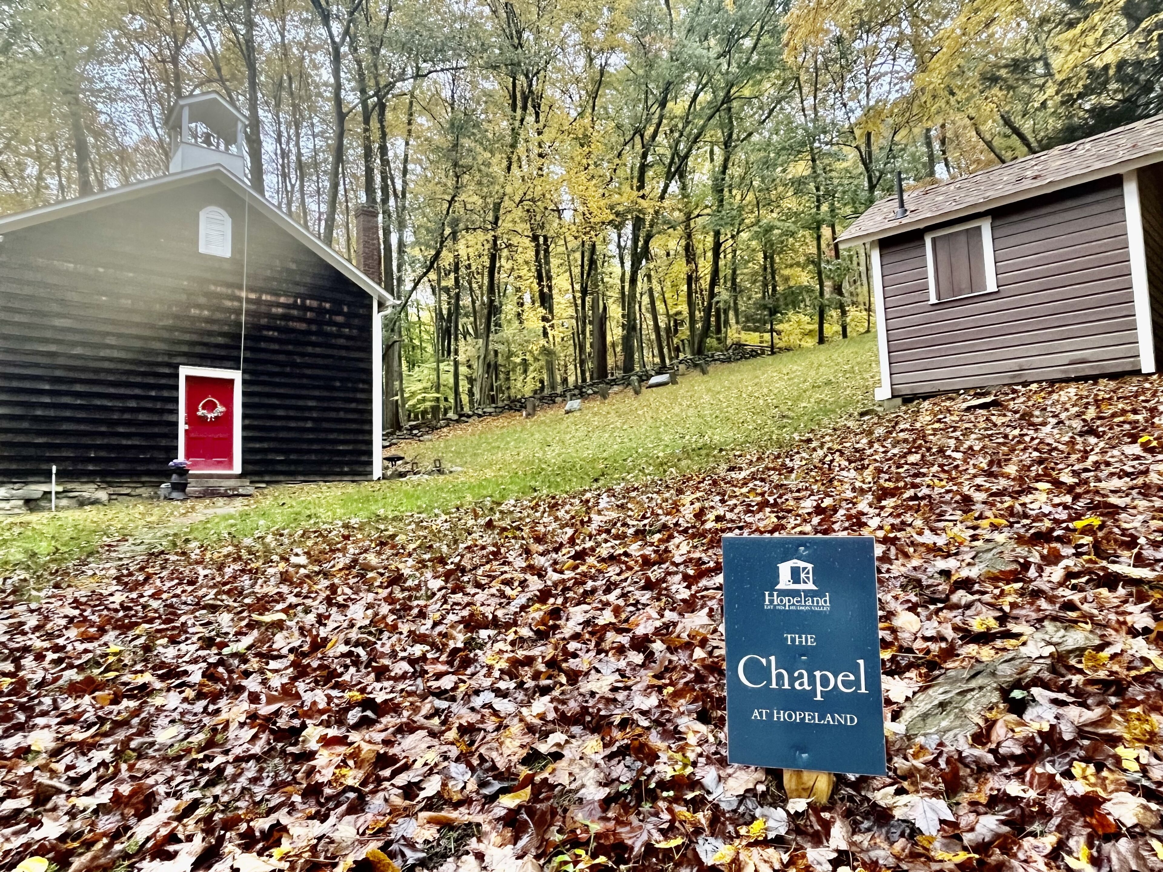A chapel at Hopeland with a red door, surrounded by autumn leaves and trees.