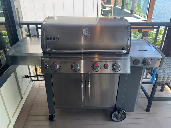 A stainless steel Weber Genesis II grill with four burners, a side shelf, and a foldable table.