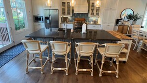 A spacious kitchen with a large island, white cabinetry, and a dining area with wicker chairs.