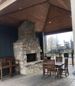 Een terras buiten met een stenen openhaard, houten banken en een tafel met stoelen.