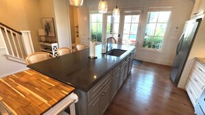 A modern kitchen with a large island, wooden dining table, and pendant lighting.