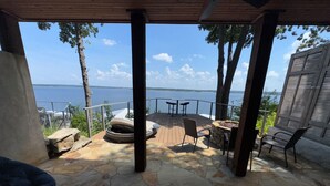 A stone patio with a hot tub, outdoor seating, and a view of the water.