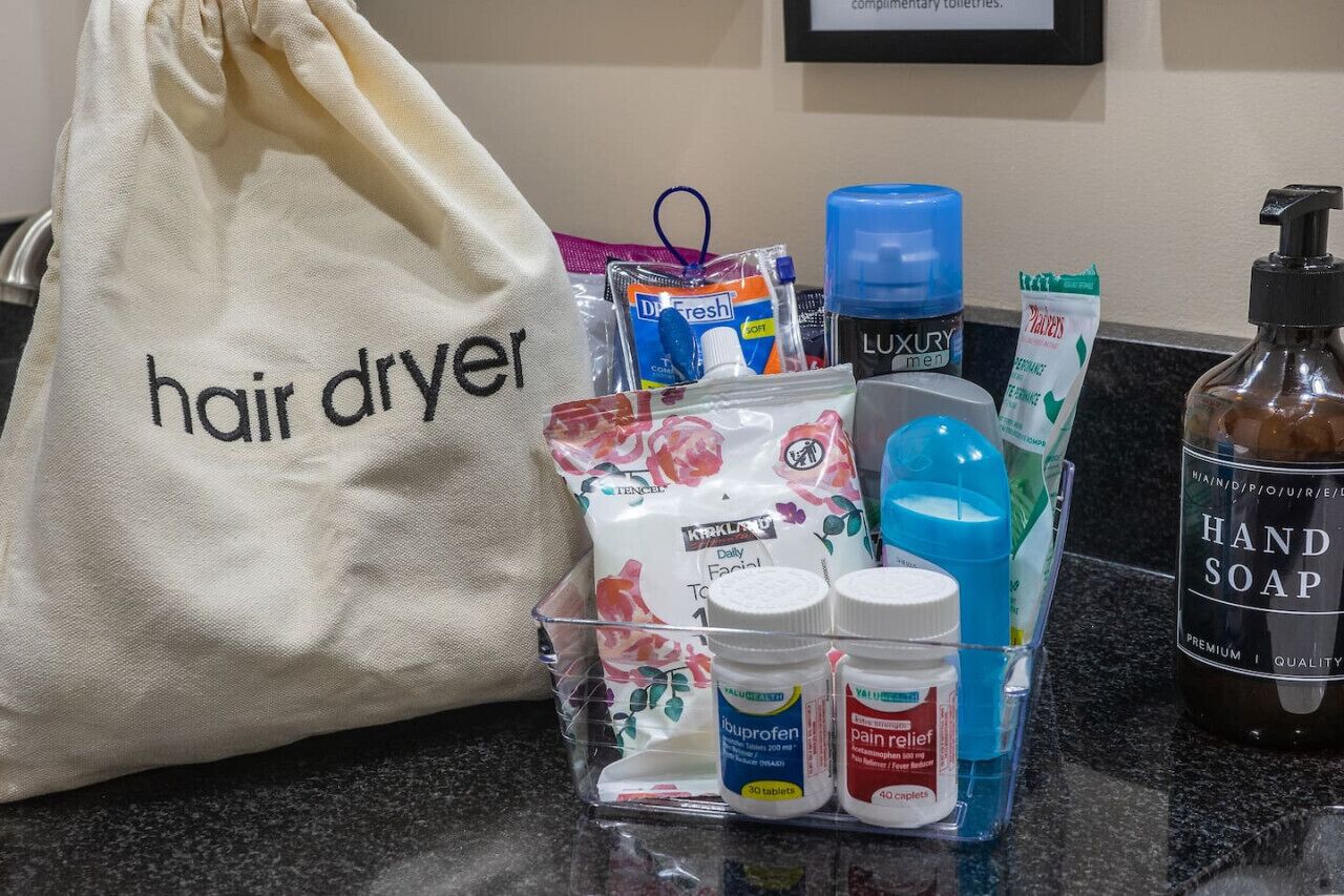 A bathroom counter with a hair dryer, toiletries, and a bottle of hand soap.