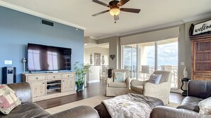 A spacious living room with a large flat-screen TV, leather sofas, and a ceiling fan. - Luxury Minorca ~ Corner Unit ~ Ocean & River Views! 2 Balconies! Paros 606 (New Smyrna Beach)