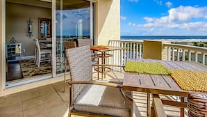 A balcony with a table and chairs, a sliding glass door, and a view of the ocean. - Luxury Minorca ~ Corner Unit ~ Ocean & River Views! 2 Balconies! Paros 606 (New Smyrna Beach)