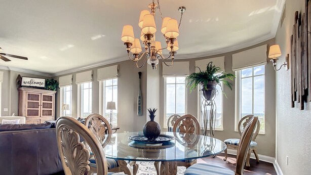 A dining area with a glass table, striped chairs, and a chandelier. - Luxury Minorca ~ Corner Unit ~ Ocean & River Views! 2 Balconies! Paros 606 (New Smyrna Beach)