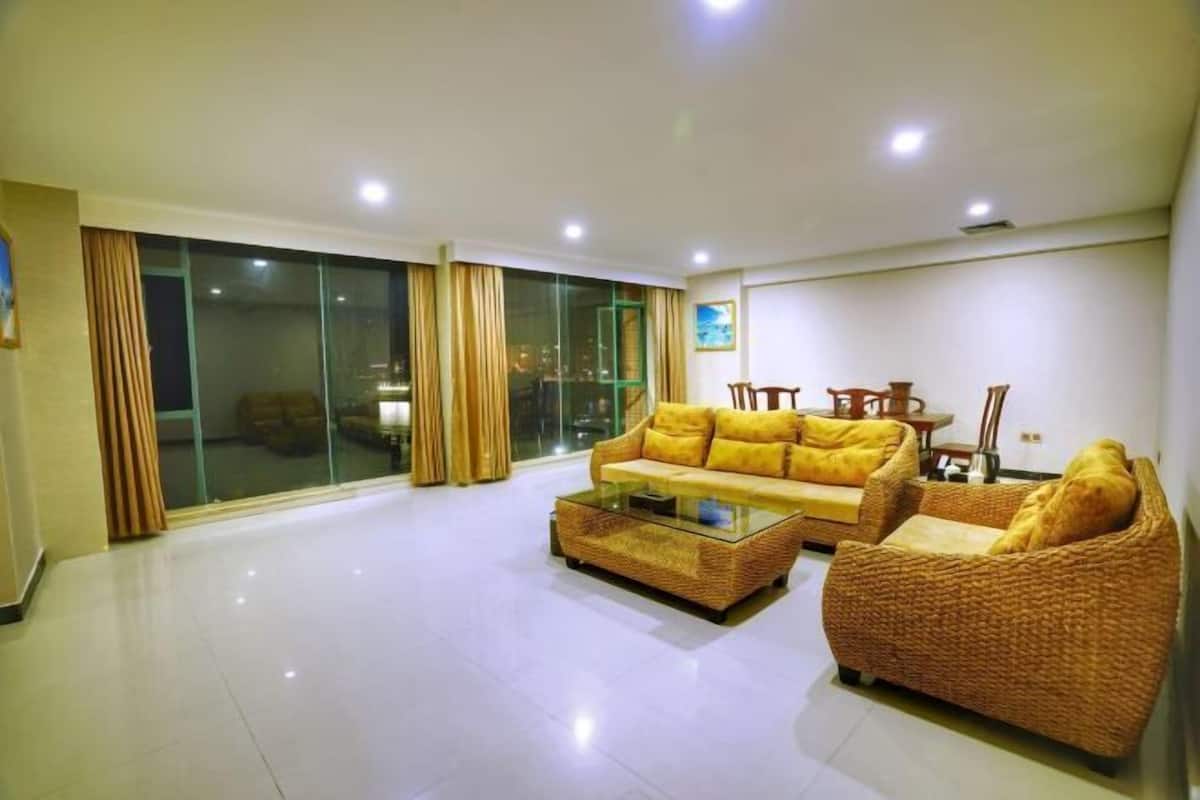 A spacious living room with a large glass door leading to a balcony, a sofa, a coffee table, and a wicker armchair.