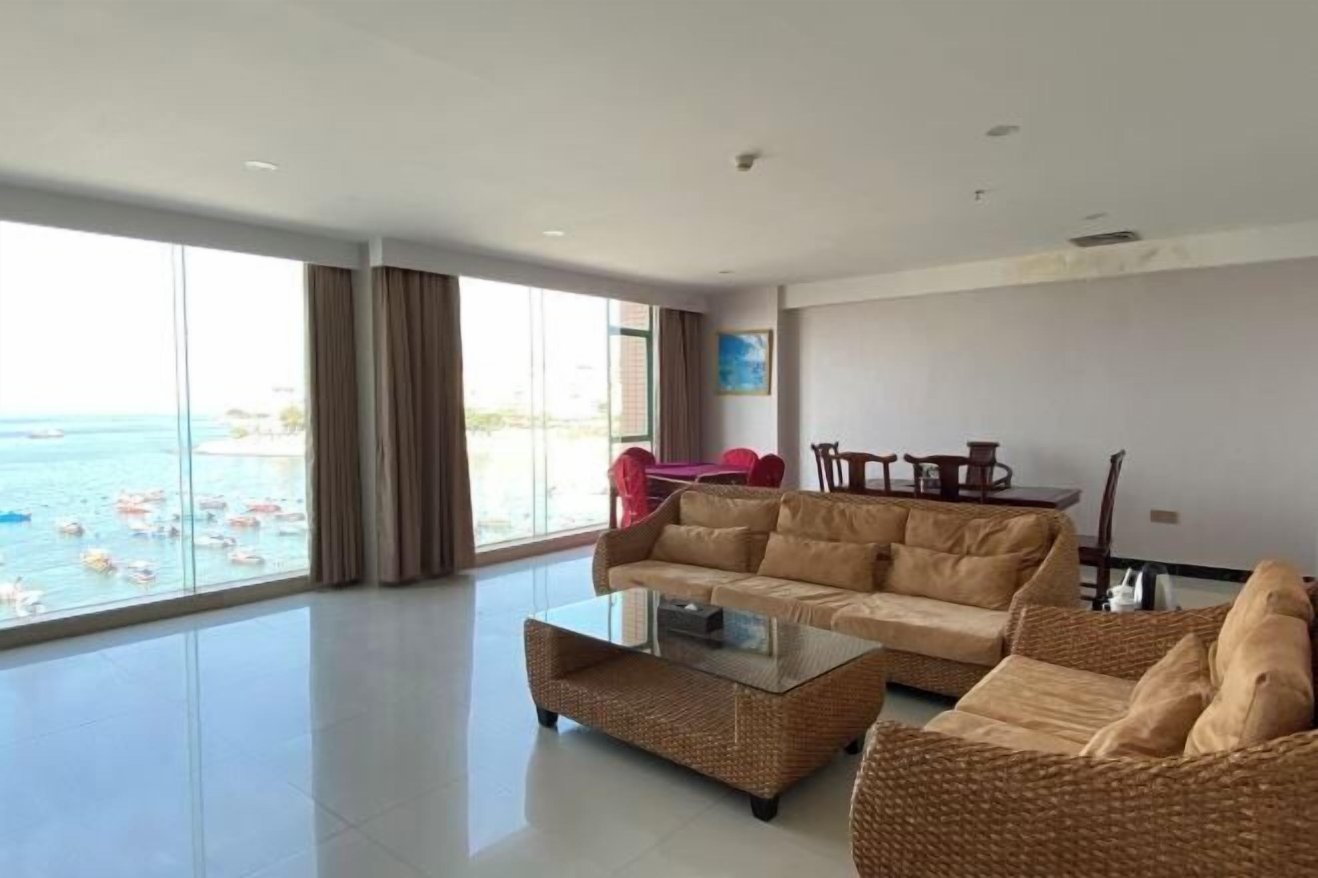 A spacious living room with a large window overlooking the sea, a sofa, a coffee table, and a dining area.