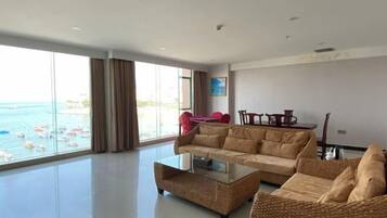 A spacious living room with a large window overlooking the sea, a sofa, a coffee table, and a dining area.