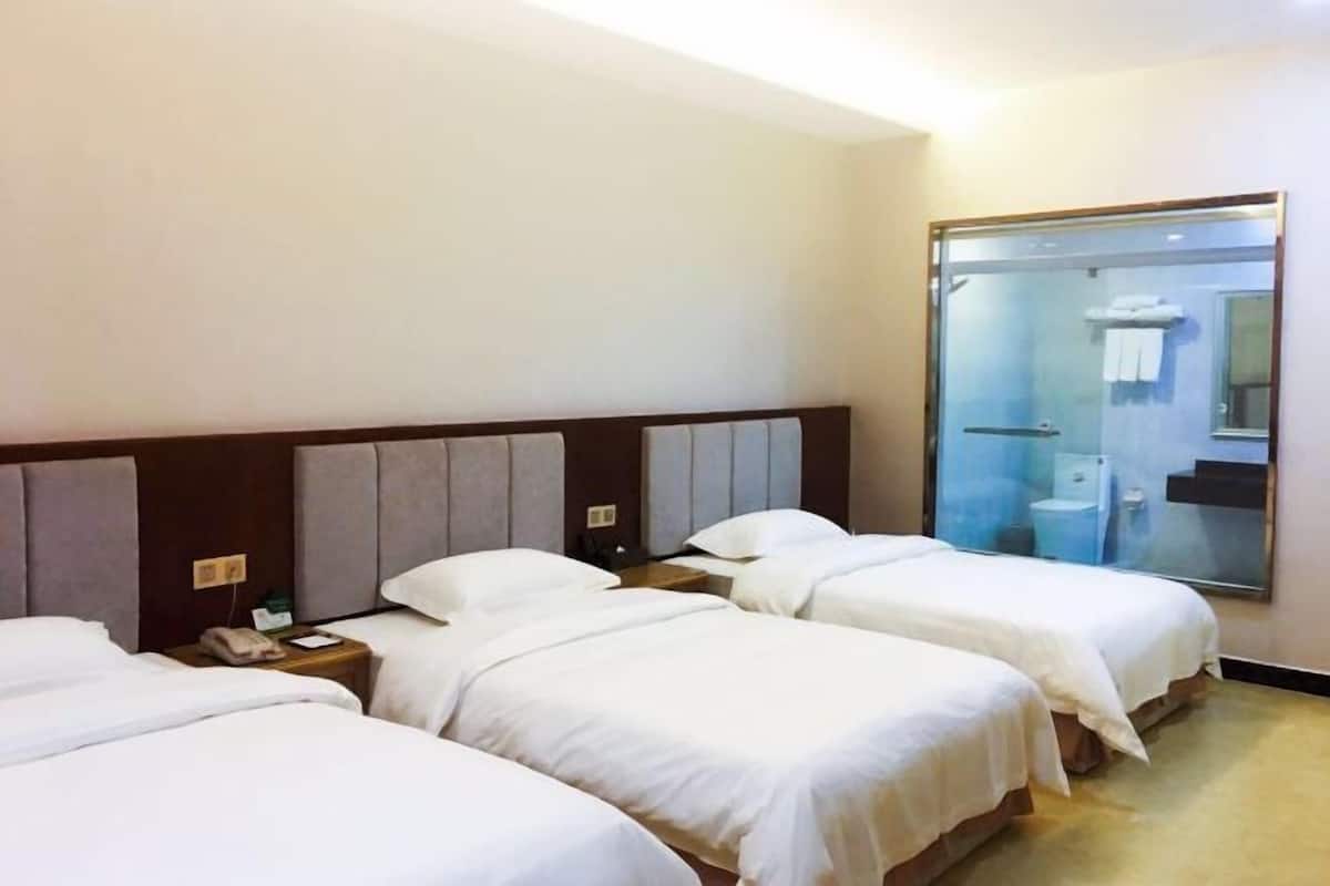 A hotel room with three beds, a large mirror, and a glass shower enclosure.